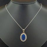 An 2.78ct Oval Blue Australian Opal with a yellow gold rubover setting and surrounded by a cluster of 0.55ct round-cut diamonds, set in white gold and on a white gold chain, hanging on the black jewellery bust.